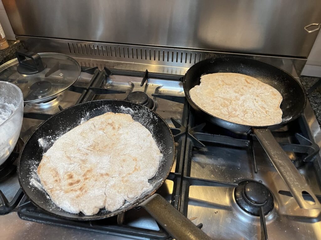 Desem panpizza's aan het bakken op het gasfornuis, beide verder gevorderd in het bakproces