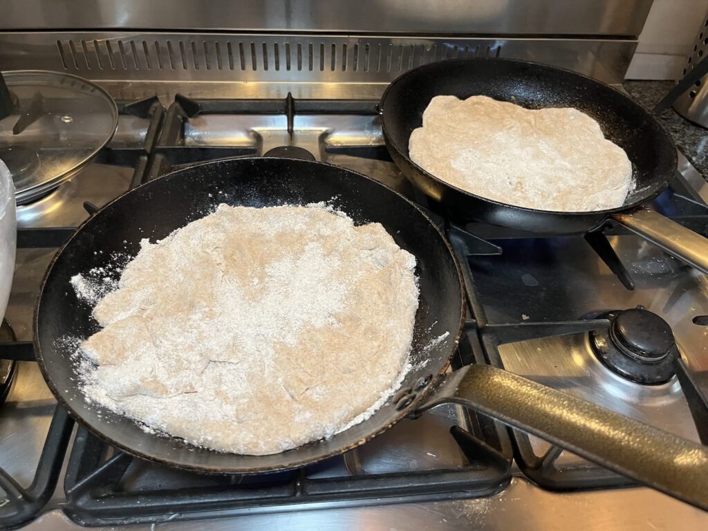 Twee uitgerolde desempizza's in gietijzeren pannen op het gasfornuis, nog ongaar